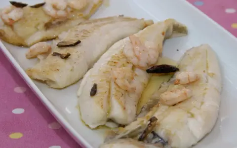 Filetes de gallo a la plancha con gambas y ajo laminado, servidos en una bandeja blanca.