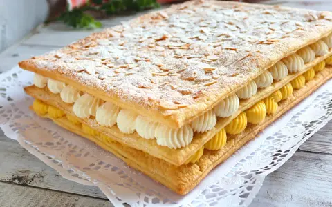 Delicioso pastel de milhojas de crema, con capas de hojaldre crujiente, crema pastelera amarilla y crema batida blanca, espolvoreado con azúcar glas y almendras laminadas.