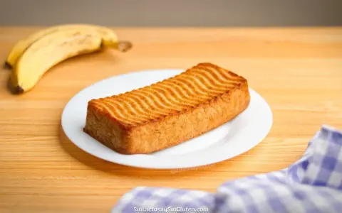 Un delicioso bizcocho de plátano con un patrón ondulado dorado en la parte superior, acompañado de plátanos maduros.