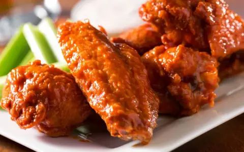 Alitas de pollo en freidora de aire, cubiertas de salsa picante, servidas con bastones de apio crujientes.