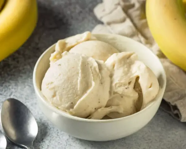 Delicioso helado de plátano cremoso en un tazón blanco, con plátanos amarillos frescos al lado.