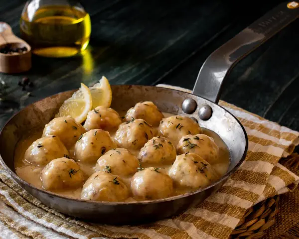Albondigas de pollo caseras en salsa cremosa, servidas en sartén con limón y hierbas.