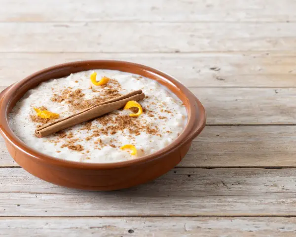 Un tazón de arroz con leche cremoso, espolvoreado con canela y adornado con cáscara de naranja y una rama de canela.