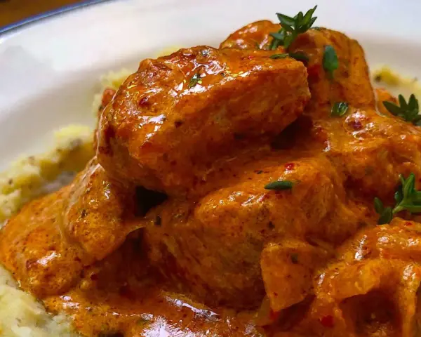 Sabroso pavo en salsa cremosa, con trozos de carne tierna y un toque de hierbas frescas, servido sobre puré de patatas.