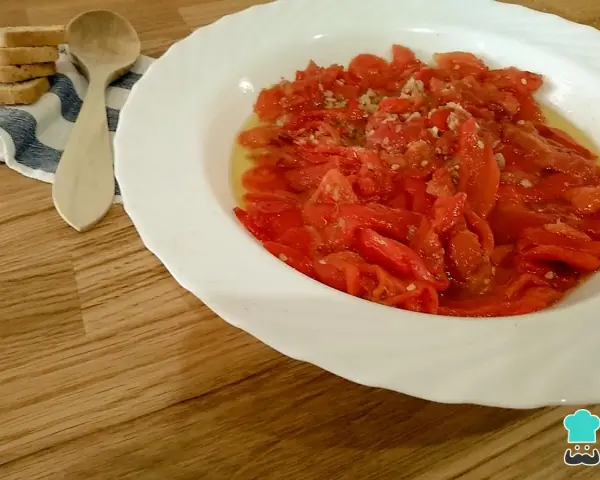 Asadillo manchego, pimientos asados con ajo y aceite, listos para disfrutar con tostadas y una cuchara de madera.