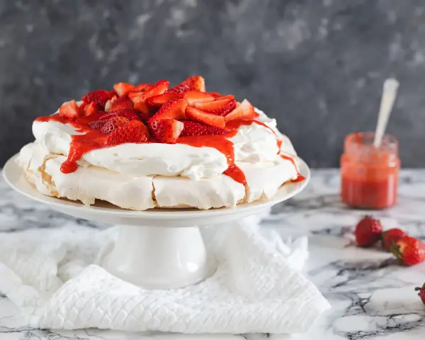 Deliciosa tarta pavlova con fresas frescas y salsa de fresa, lista para ser disfrutada.