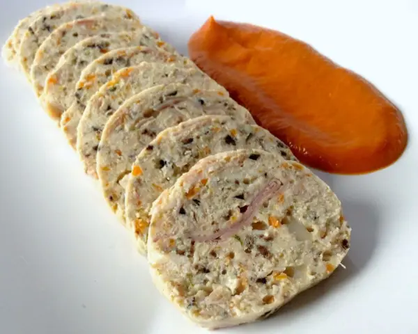 Fiambre de pollo casero en rodajas, con trocitos de verdura y jamón, acompañado de una salsa naranja.