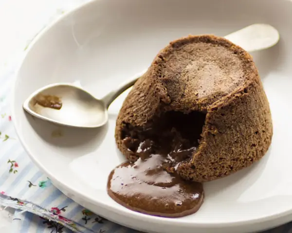 Coulant de chocolate recién hecho, con su interior líquido y cremoso desbordándose. Una cuchara plateada espera pacientemente.