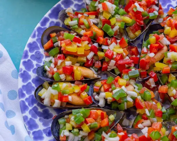 Mejillones a la vinagreta, cubiertos con una colorida mezcla de pimientos picados y cebolla.