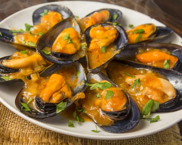 Mejillones en salsa, humeantes y listos para disfrutar. Un plato delicioso con un toque de perejil fresco.