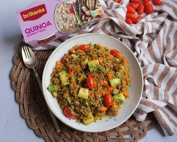Un plato de quinoa con verduras, incluyendo tomates cherry, calabacín y zanahoria, listo para disfrutar.