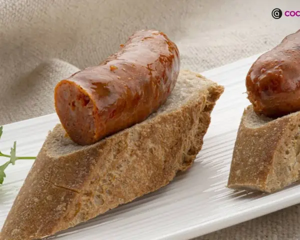 Chorizo a la sidra jugoso sobre pan rústico, decorado con perejil fresco. Un bocado delicioso.