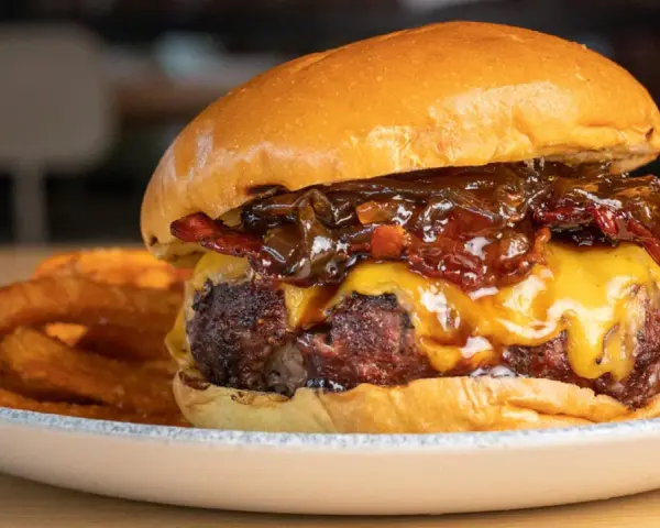 La mejor receta de hamburguesas caseras: jugosa carne, queso fundido, cebolla caramelizada y crujientes patatas fritas.