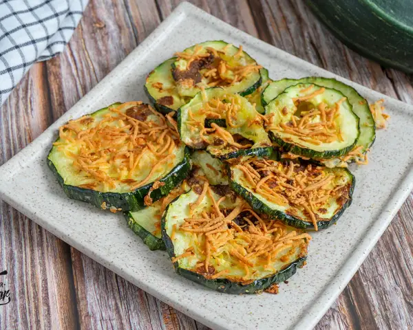 Rodajas de calabacín en freidora de aire, doradas y crujientes, con un toque de queso rallado. ¡Una delicia saludable!