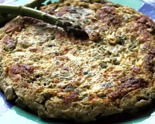 Tortilla de esparragos dorada y esponjosa, con espárragos frescos encima, servida en un plato azul.
