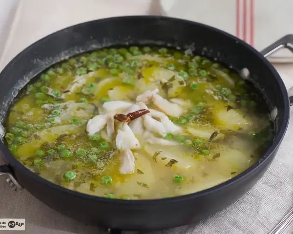 Patatas en salsa verde con trozos de pescado blanco y guisantes, servido en una sartén.