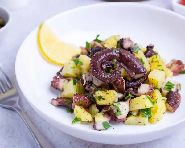 Ensalada de pulpo y patatas, un ejemplo de recetas sanas con pulpo. Servida en plato blanco con limón y perejil.