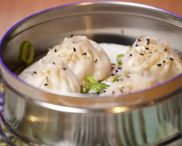 Deliciosos dumplings al vapor, cubiertos con semillas de sésamo y cebolleta, servidos en una vaporera metálica.