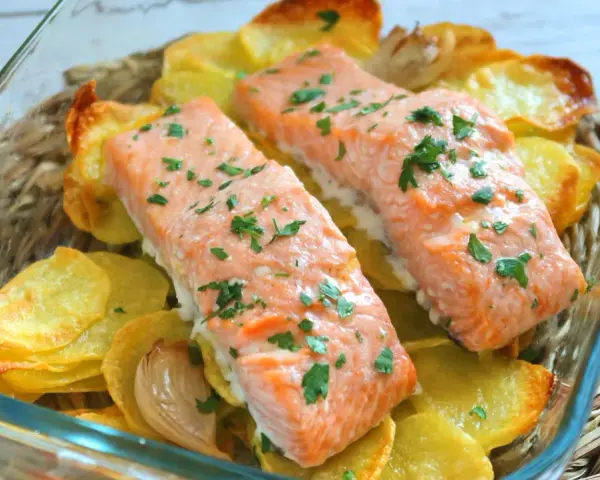 Dos filetes de salmón al horno con patatas crujientes y perejil picado, servidos en una fuente de vidrio.
