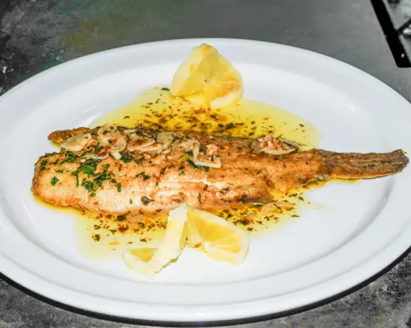 Delicioso lenguado a la meunière, bañado en mantequilla dorada, ajo y perejil, con gajos de limón.