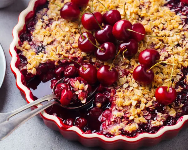 Delicioso postre con cerezas, cubierto de crumble dorado y adornado con cerezas frescas.