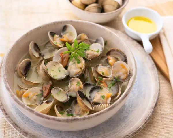 Deliciosos tipos de berberechos cocinados en su jugo, servidos en un cuenco de cerámica con perejil picado.