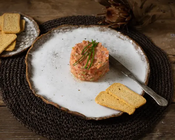 Delicioso tartar de tomate, servido con tostas crujientes y un cuchillo de plata. Un plato fresco y vibrante.