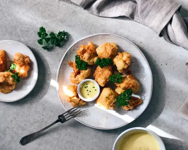 Crujientes trozos de coliflor rebozada, servidos con una cremosa salsa y decorados con perejil fresco. ¡Un aperitivo delicioso!