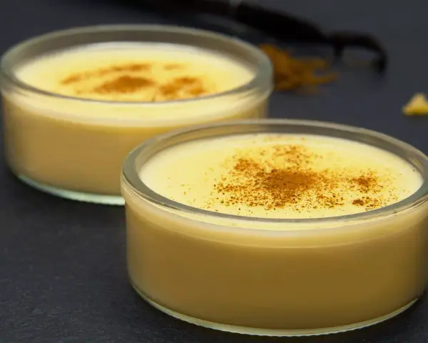 Dos cuencos de natillas caseras, espolvoreadas con canela, junto a palitos de canela y vainilla.