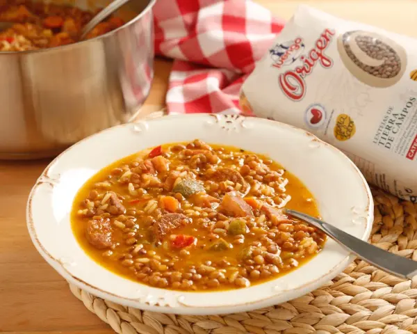 Plato de lentejas con arroz, chorizo y verduras. Una bolsa de lentejas "Origen" a un lado.
