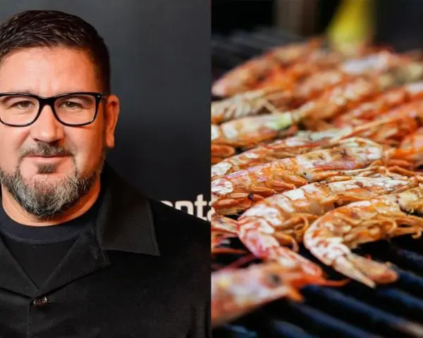 Hombre con gafas y barba junto a una parrilla llena de cigalas a la plancha, listas para ser degustadas.