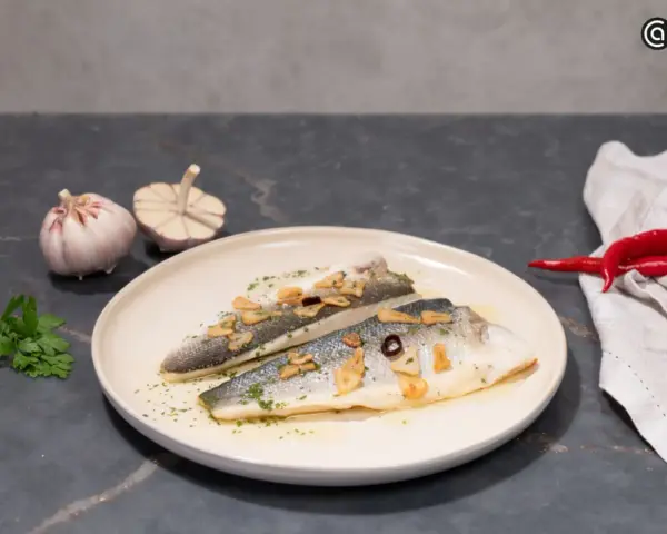 Dos filetes de lubina a la donostiarra, con láminas de ajo dorado, perejil picado y un toque de guindilla.