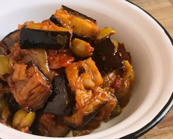 Un plato de caponata siciliana, con berenjenas, aceitunas y tomate, servido en un cuenco blanco.