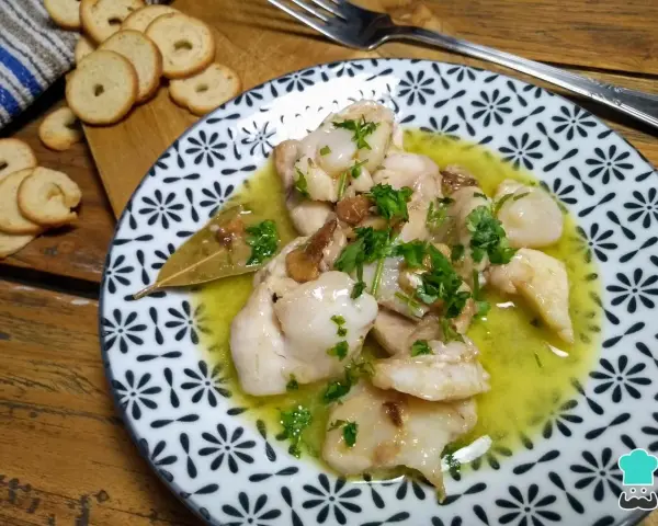 Plato de que son las cocochas de bacalao, tiernas y jugosas, en una salsa amarilla con perejil picado y galletas tostadas al lado.