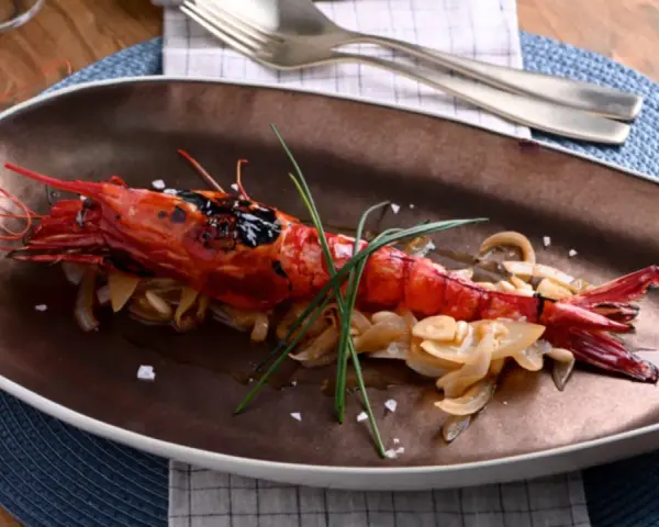 Un langostino rojo a la parrilla, servido sobre cebolla caramelizada y adornado con cebollino. Un plato que evoca la pregunta: ¿qué son los carabineros?