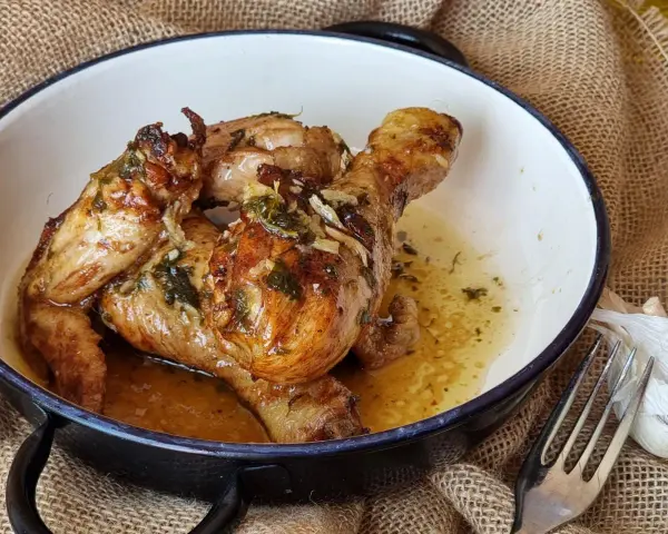 Sabroso pollo al ajillo dorado y jugoso, servido en una cazuela con su jugo y hierbas.