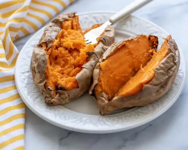 Boniato tierno y esponjoso hecho en air fryer, servido en plato blanco con un tenedor.