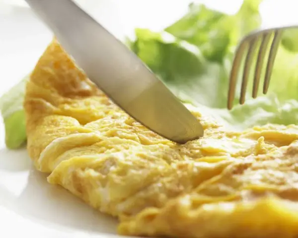 Un cuchillo corta una dorada tortilla francesa servida con hojas de lechuga fresca.
