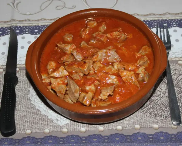 Un cuenco de barro rebosante de magro con tomate, listo para ser disfrutado con pan y vino tinto.