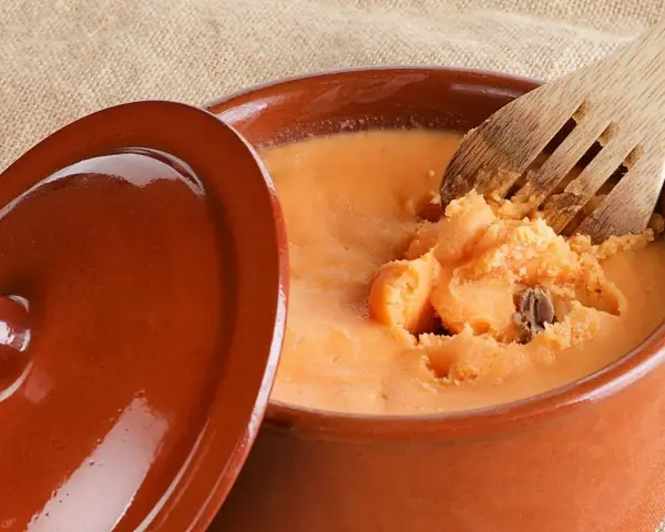 Un cuenco de barro con lomo en manteca, listo para ser servido. Una cuchara de madera remueve la deliciosa preparación.