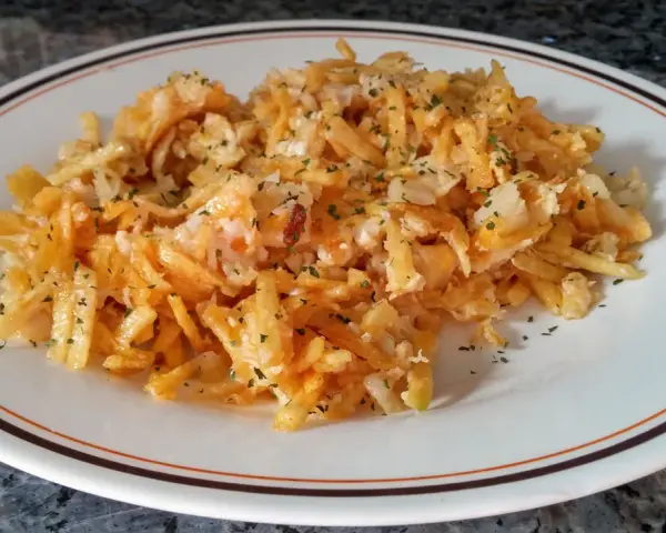 Bacalao dorado desmenuzado con patatas fritas finas y perejil picado, servido en un plato blanco con borde marrón y naranja.
