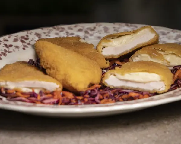 Pechuga villaroy dorada y crujiente, rellena de queso fundido, servida sobre una ensalada de col morada y zanahoria.