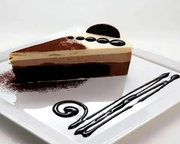 Deliciosa tarta de tres chocolates, con capas de mousse de chocolate blanco, con leche y negro, decorada con cacao y un toque de galleta.