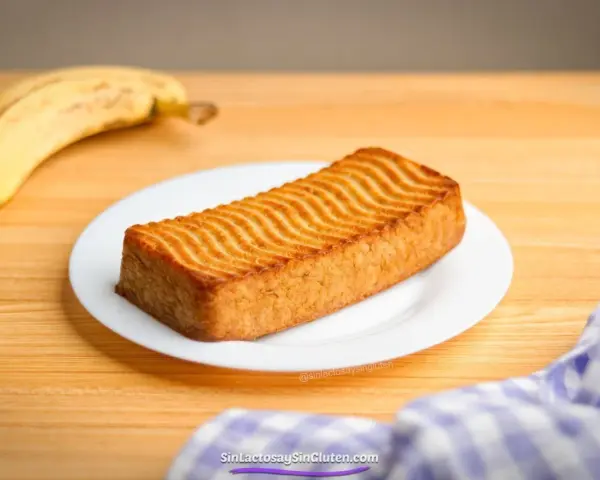 Un delicioso bizcocho de plátano con un patrón ondulado dorado en la parte superior, acompañado de plátanos maduros.