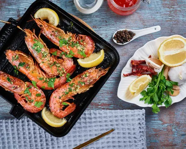 Deliciosos langostinos a la plancha, servidos con rodajas de limón y perejil fresco. Acompañados de ajo, guindillas y granos de pimienta.