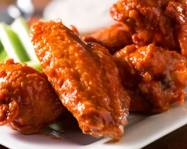 Alitas de pollo en freidora de aire, cubiertas de salsa picante, servidas con bastones de apio crujientes.
