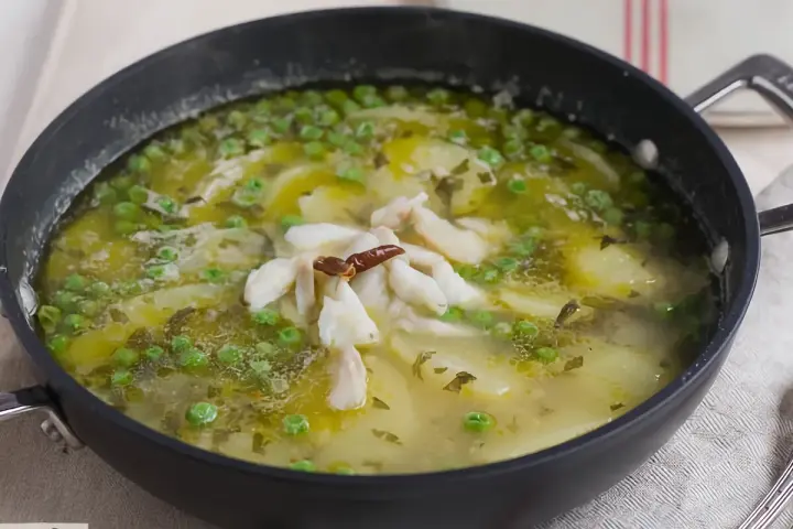 Patatas en salsa verde con trozos de pescado blanco y guisantes, servido en una sartén.