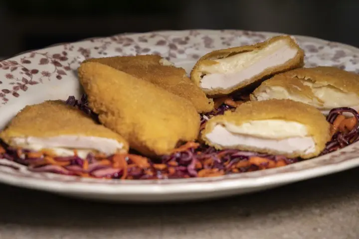 Pechuga villaroy dorada y crujiente, rellena de queso fundido, servida sobre una ensalada de col morada y zanahoria.