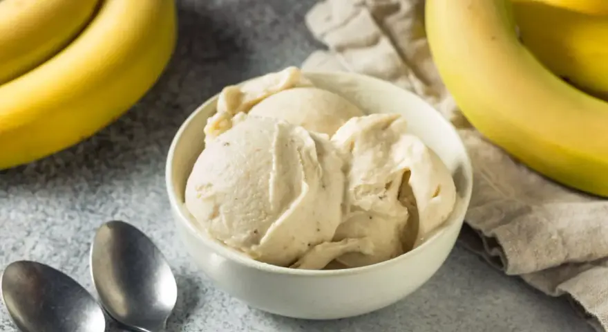 Delicioso helado de plátano cremoso en un tazón blanco, con plátanos amarillos frescos al lado.