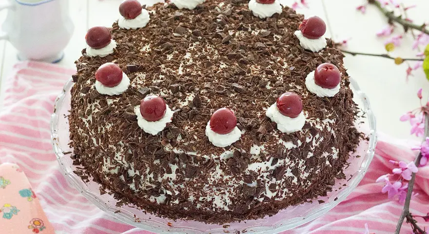 Deliciosa tarta Selva Negra, cubierta de virutas de chocolate y coronada con cerezas y nata.
